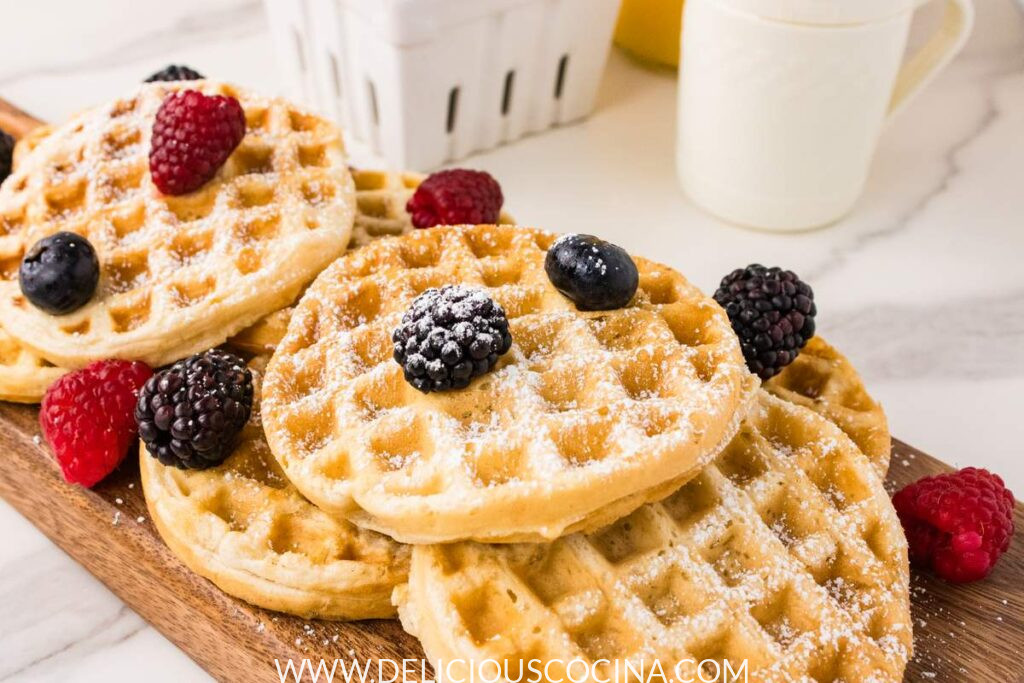 Several mini waffles topped with berries and powdered sugar on a wooden board