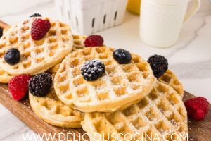 Several mini waffles topped with berries and powdered sugar on a wooden board