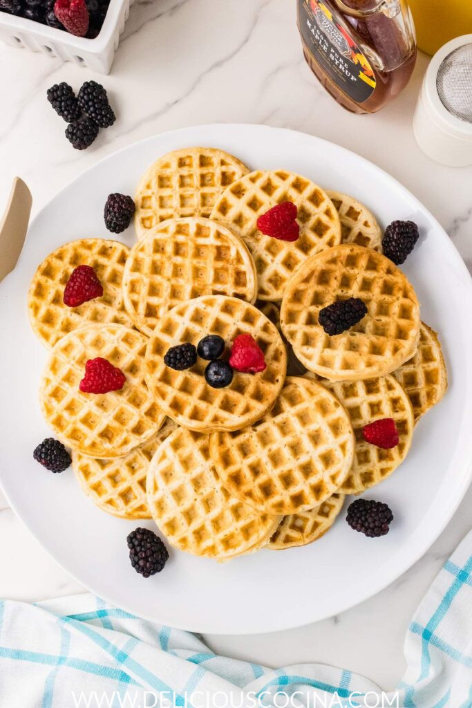A white platter full of mini vegan waffles topped with blueberries and raspberries