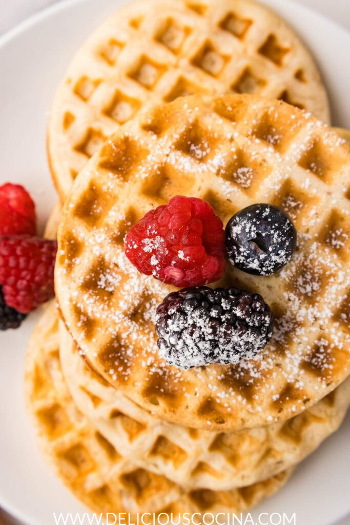 Close up of several waffles topped with berries and some powdered sugar