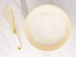 Dry ingredients for waffles in a white bowl with a whisk on the side