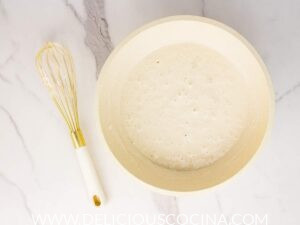 Vegan waffle batter in a white bowl with a whisk on the side