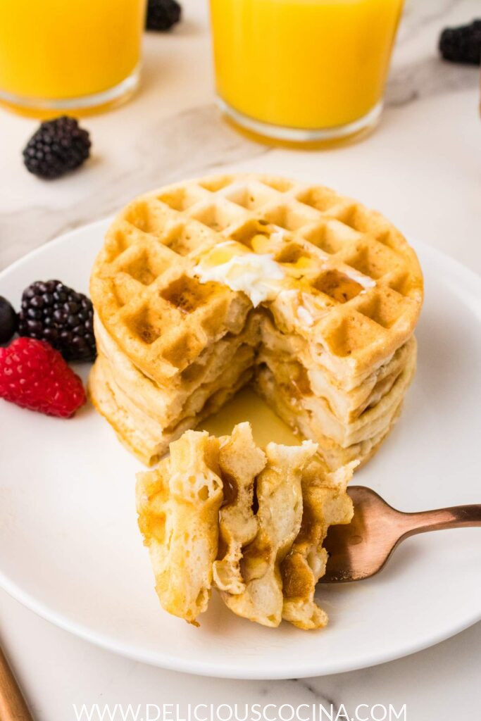 A plate with stack of waflles, with a bite size piece cut out and on a fork
